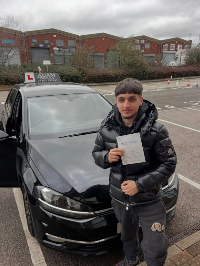 Student holding their driving test pass certificate beside the Adam Driving School car