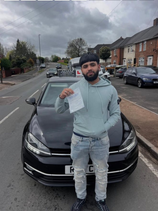 Student holding their driving test pass certificate beside the Adam Driving School car