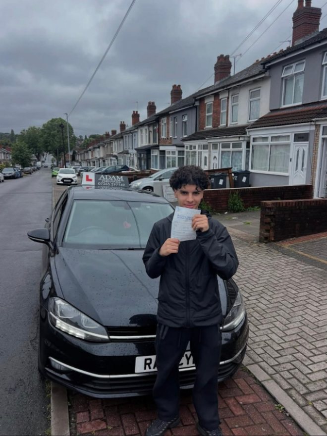 Student holding their driving test pass certificate beside the Adam Driving School car